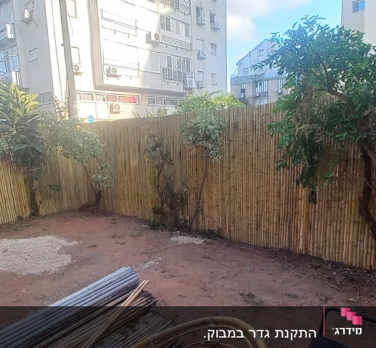 גדר במבוק עם צמחים, צינור מים וחומרי בנייה